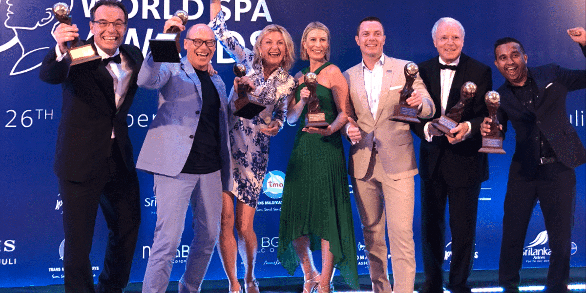 Gewinner*Innen des World Spa Awards posieren jubelnd mit Pokal auf Bühne für Fotografen
